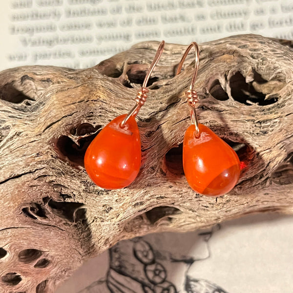 Pair of orange earrings on a textured wooden surface with a blurred background
