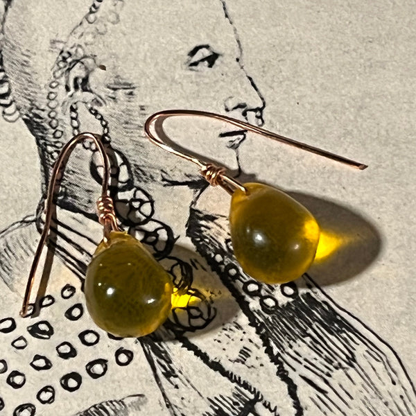 gold amber color teardrop earrings on a textured surface with black and white design