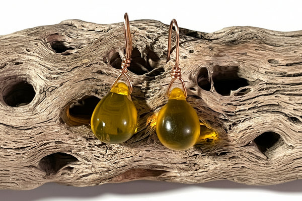 Yellow glass earrings on a piece of driftwood with text in the background