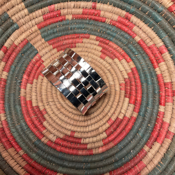 Close-up of a woven mat with concentric circles in red, blue, and beige, featuring a metallic object in the center.