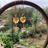 Pair of amber-colored earrings hanging from a rustic metal arch with a garden background.