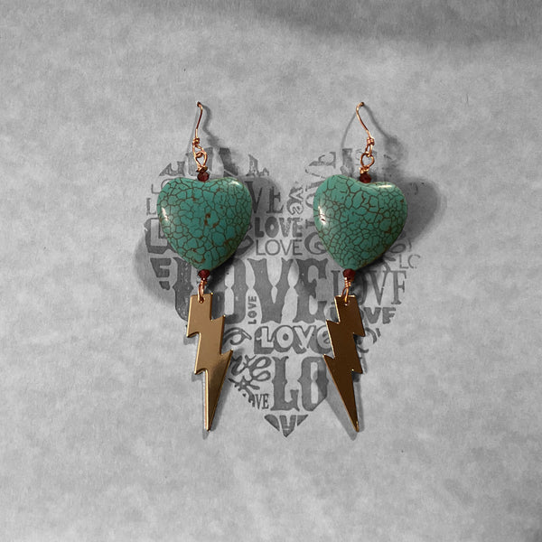 Heart-shaped turquoise earrings with lightning bolt charms on a textured gray background.