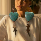 Person wearing turquoise heart-shaped earrings with lightning bolt charms.