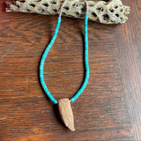 Turquoise beaded necklace with a wooden pendant on a wooden surface
