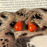 Pair of orange earrings on a piece of driftwood with text and butterfly illustration in the background