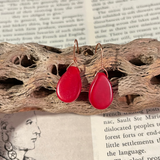 Red teardrop earrings on a piece of driftwood with text in the background