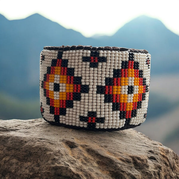 large beaded bracelet set in mountain background on a rock with rhombus pattern handcrafted bracelet white red orange and black seed beads with leather stormie bracelet cuff 7 inches length and 2 inches wide